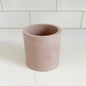 A minimalist, open-top cylindrical planter in a dusty rose pink color, set on a white marble countertop with a white subway tile backsplash.